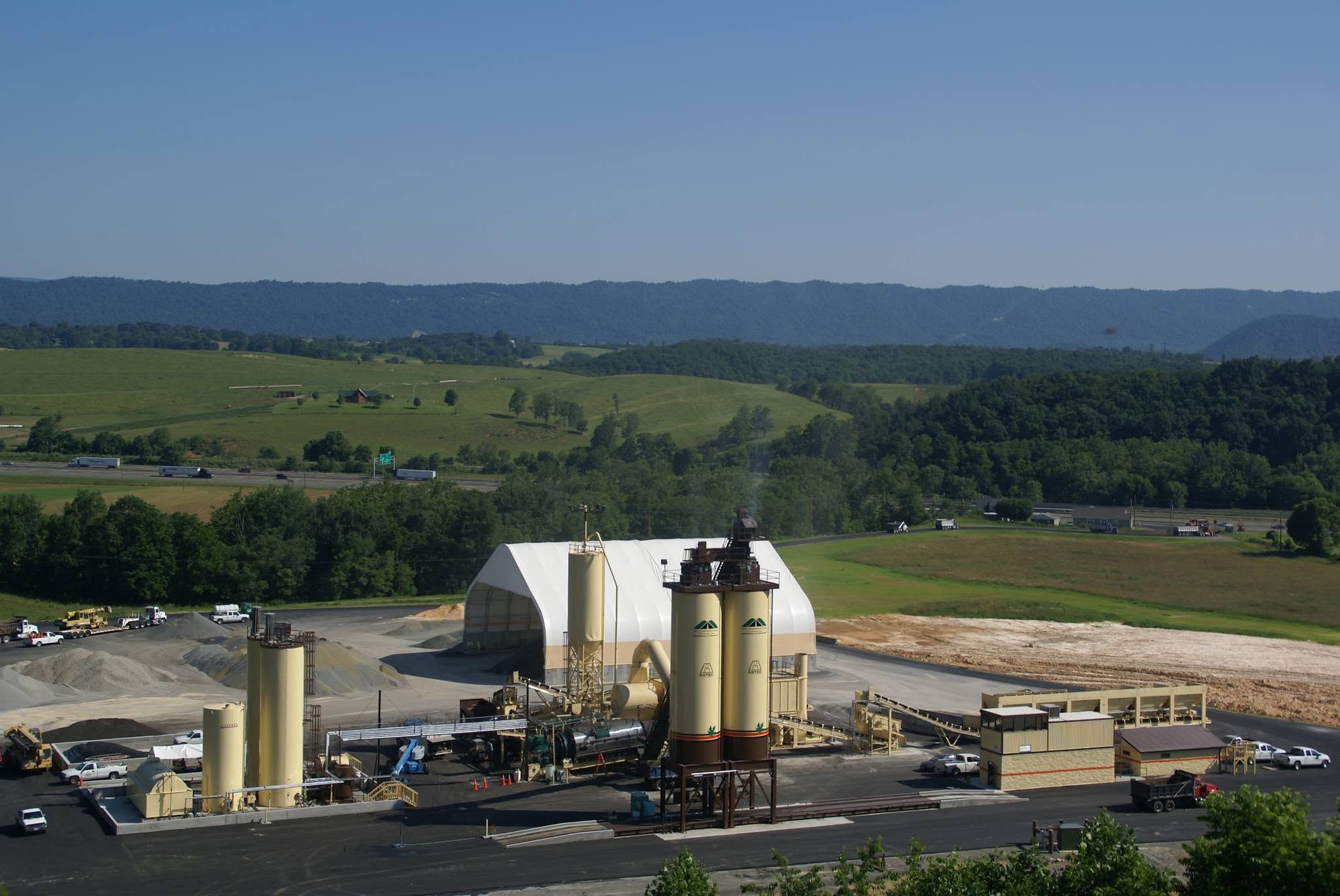 W-L asphalt plant with silos and a storage dome in a mountain valley beside an interstate highway